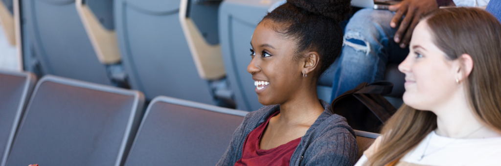 Close up image of a student sitting in a lecture hall smiling as she looks at what's in front of her.