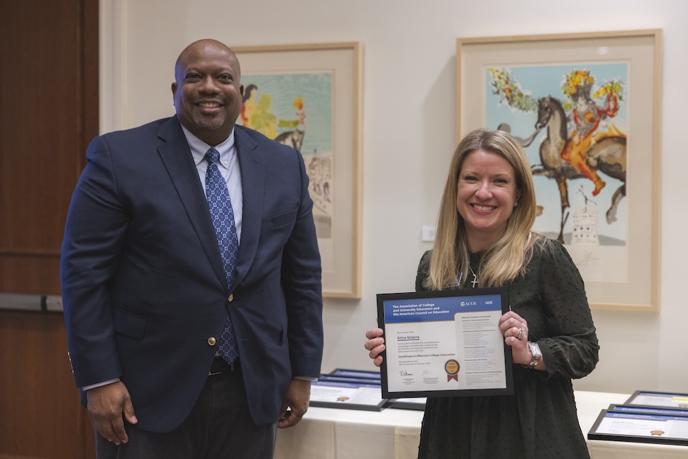Woman posing for a photo holding a certificate in her hand, with a gentleman standing off to the side smiling.
