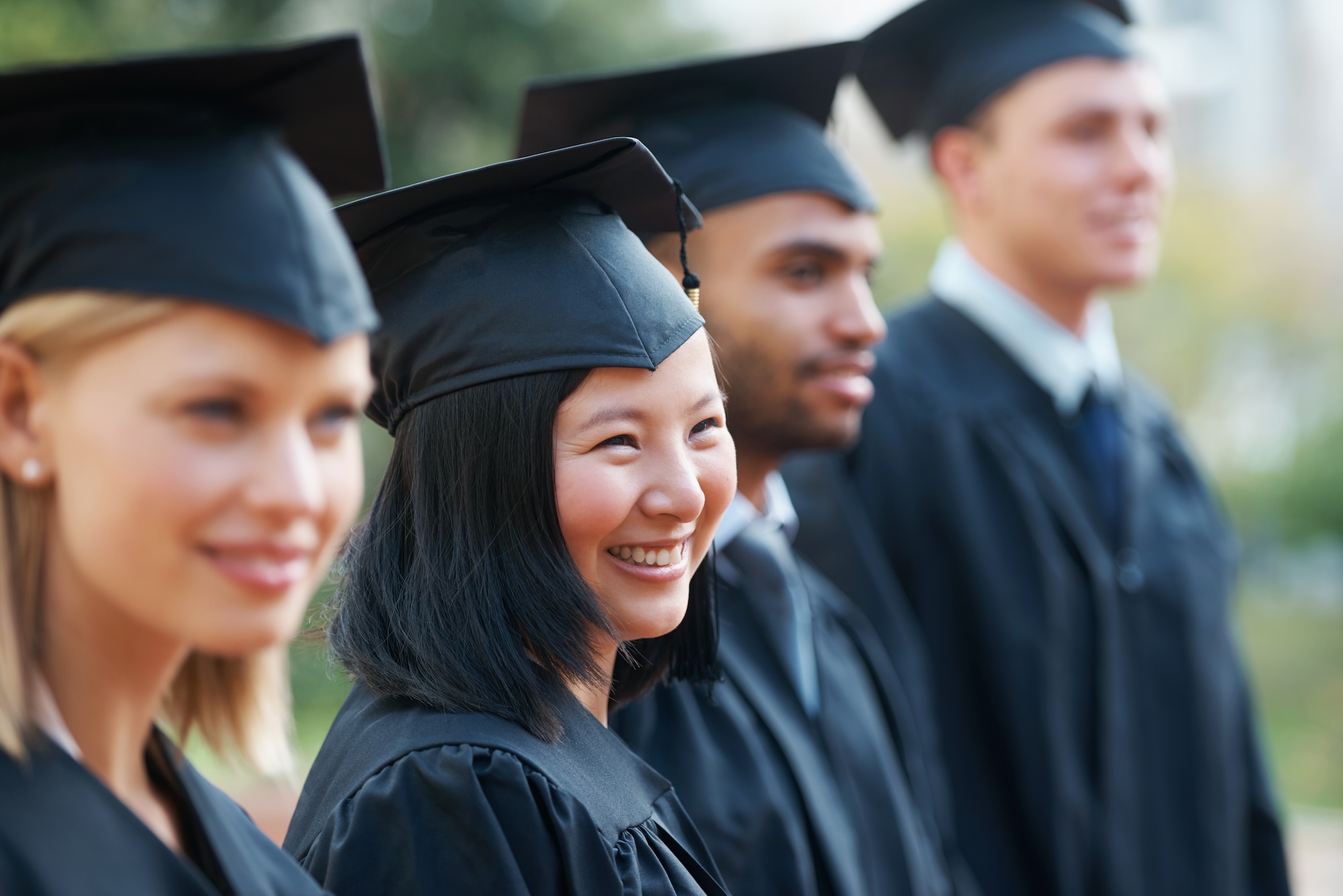 Young college graduates holding their diplomas while standing in a row and smiling