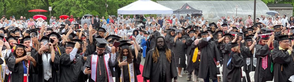 Large group of UCNJ graduates at commencement preparing to flip their mortar board tassel