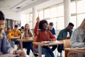 Happy student raising her hand to ask a question during lecture in the classroom.