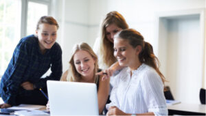 Group of students gathered around a student sitting with a laptop. 