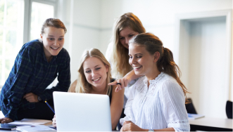 Group of students gathered around a student sitting with a laptop.
