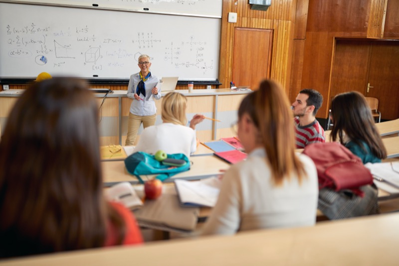 A female professor giving a lecture to students in the university amphitheater. Smart young people study at the college. Education, college, university, learning and people concept