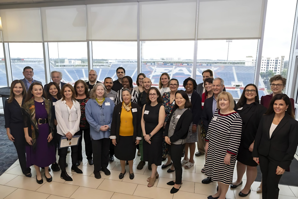 Group photo of FAU faculty posing in front of a window overlooking a football stadium.