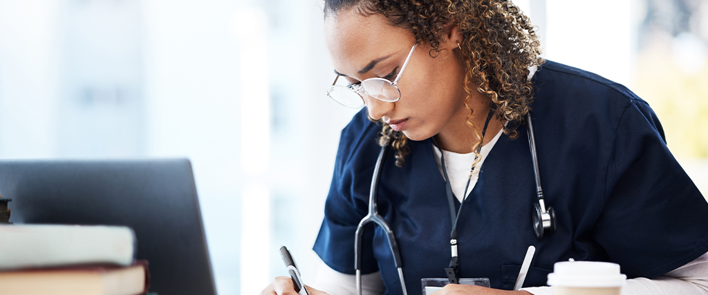 Future nurse training and researching at a desk. Writing something with pen in front of computer